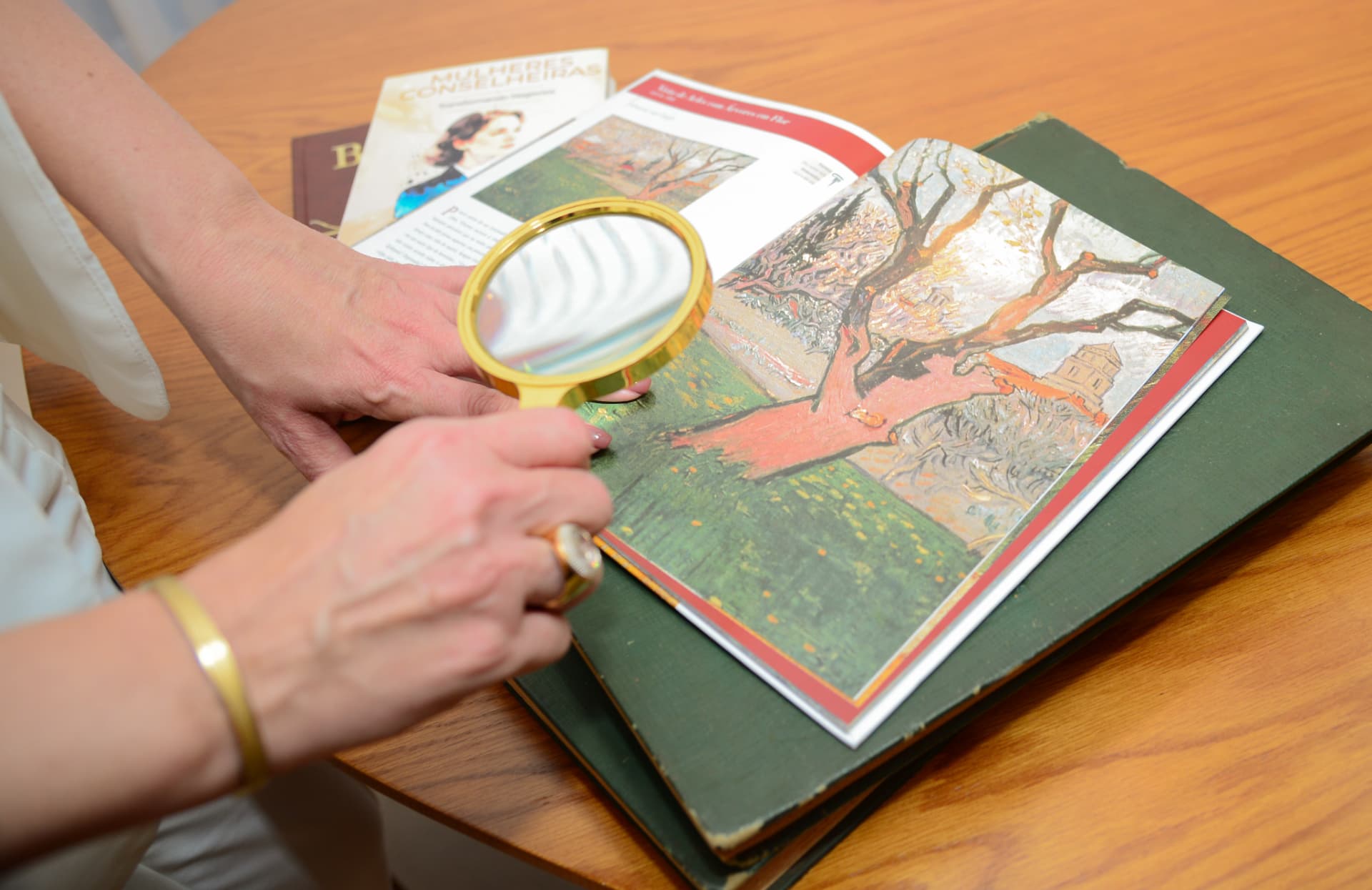 Mãos de Rejane Duarte com lupa sobre a imagem de uma árvore em um livro