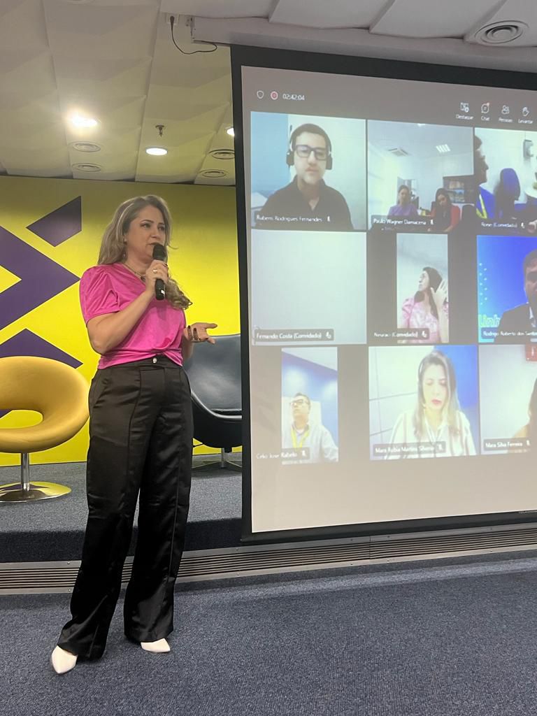 Rejane Duarte apresentando em formato híbrido com participantes remotos em telão